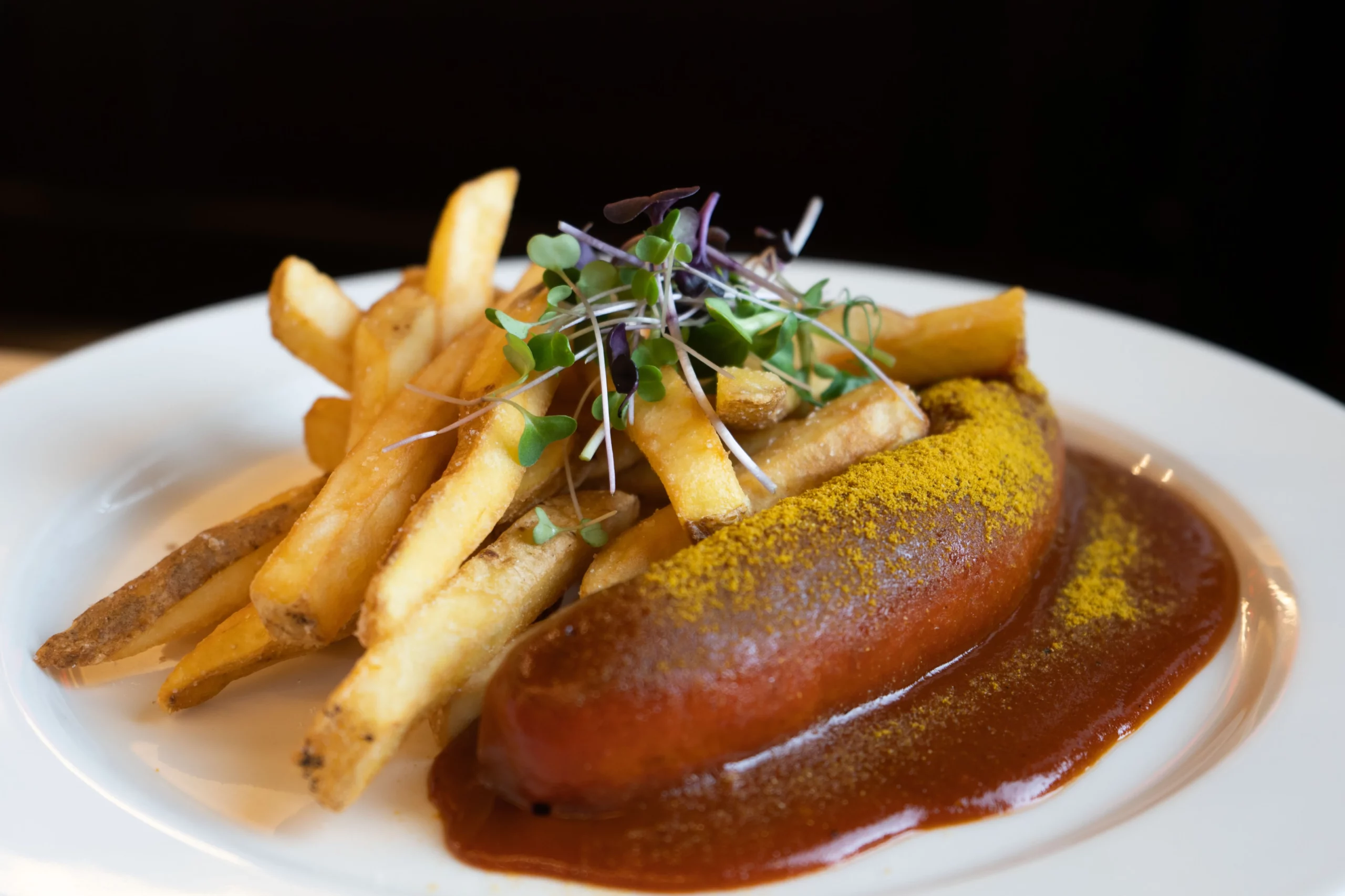 Currywurst mit Pommes frites auf einem weißen Teller, garniert mit Kresse.