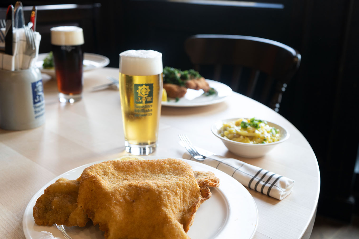 Ein Wirtshaustisch mit einem frisch gezapften Bier, einem panierten Schnitzel auf einem Teller und Besteck.