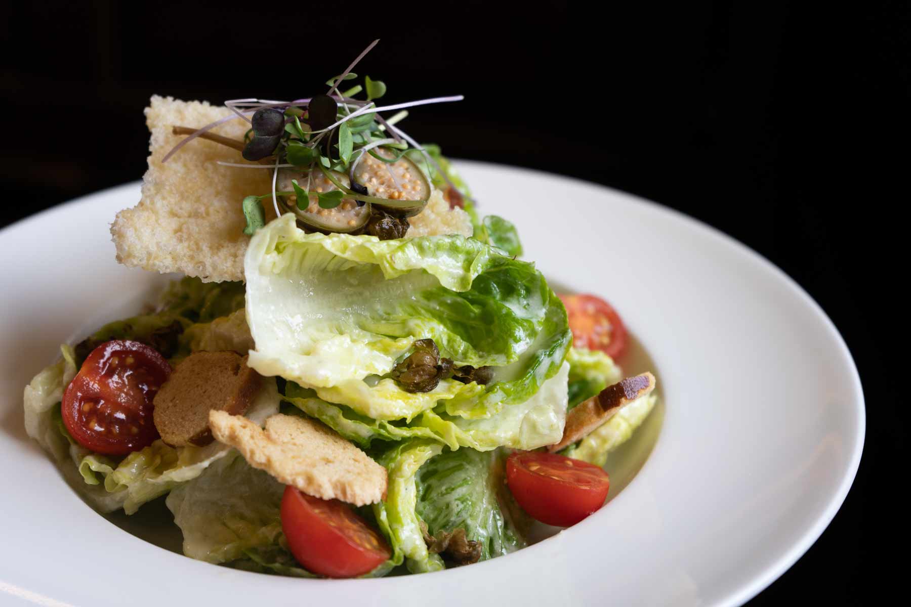 Ein frischer grüner Salat mit Tomaten, Croutons und Kräutern in einer weißen Schüssel.