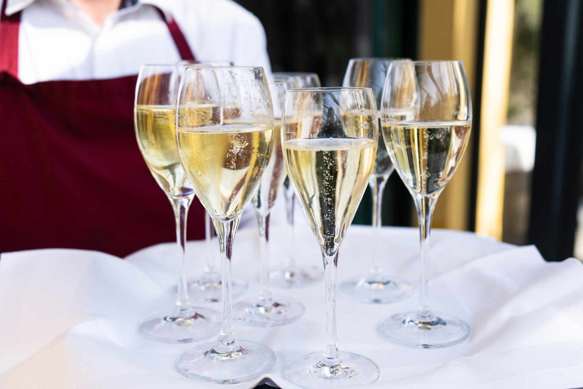 Ein Tablett mit mehreren gefüllten Champagnergläsern, das von einer Servicekraft getragen wird.