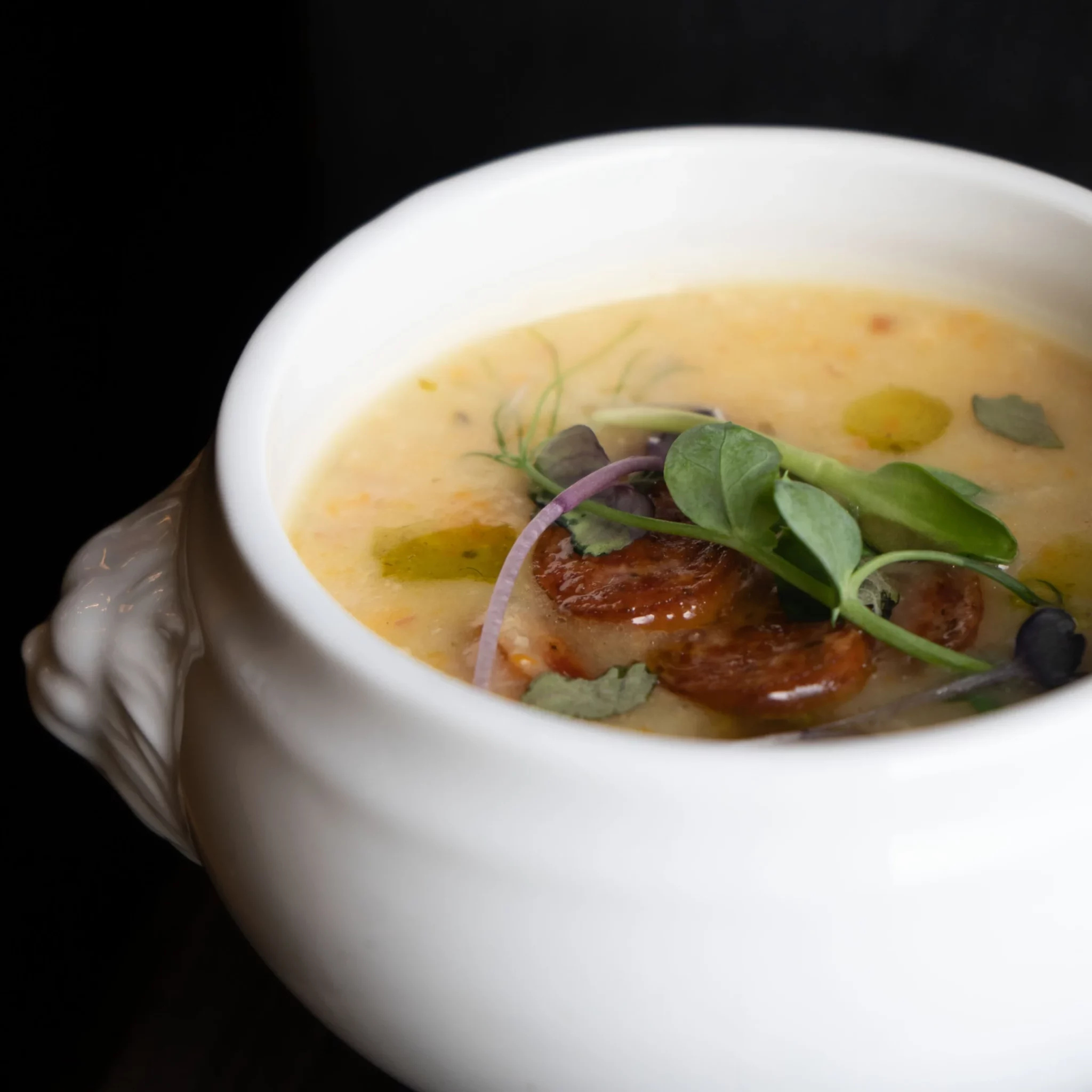 Eine feine, cremige Suppe mit Kräuter- und Gemüsebeilage in einer klassischen weißen Suppenterrine.